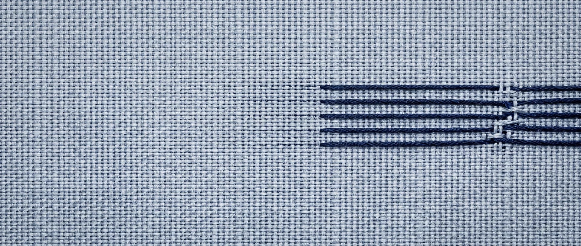 Navy threads running through finely woven pale grey-blue cloth, gathering toward the right